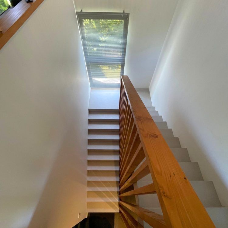 Détail de l'escalier intérieur, montrant la combinaison harmonieuse du bois, de l'acier et du béton ciré.
