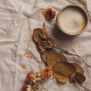 Une tasse de café posée sur un lit douillet, décorée d'une feuille morte, évoquant une ambiance cosy d'automne.